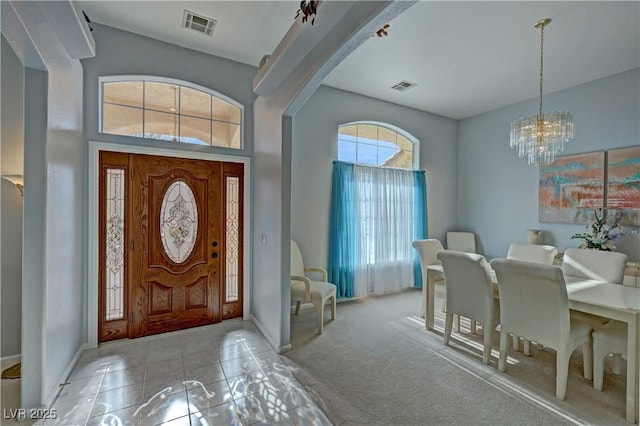 tiled foyer featuring carpet floors, an inviting chandelier, visible vents, and arched walkways