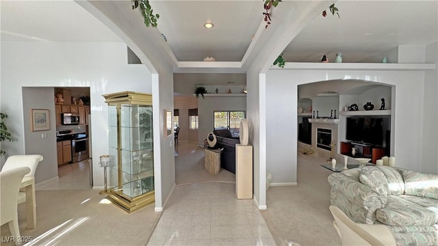 interior space featuring baseboards, arched walkways, a raised ceiling, light colored carpet, and a fireplace