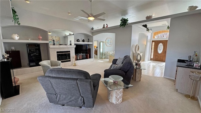 carpeted living area with arched walkways, beverage cooler, ceiling fan, and a tiled fireplace