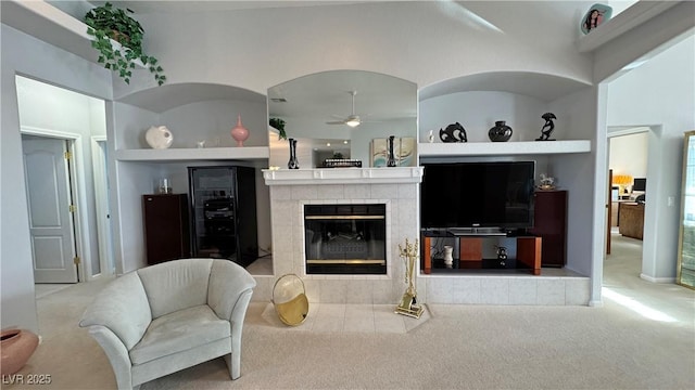 carpeted living room featuring a ceiling fan, a tile fireplace, and built in shelves