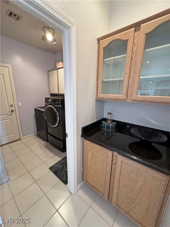 kitchen with light tile patterned floors, visible vents, washer and clothes dryer, dark countertops, and glass insert cabinets