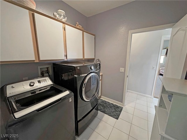 clothes washing area with light tile patterned floors, washer and clothes dryer, cabinet space, and baseboards