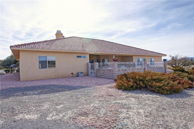 back of property featuring a tiled roof, a chimney, and stucco siding