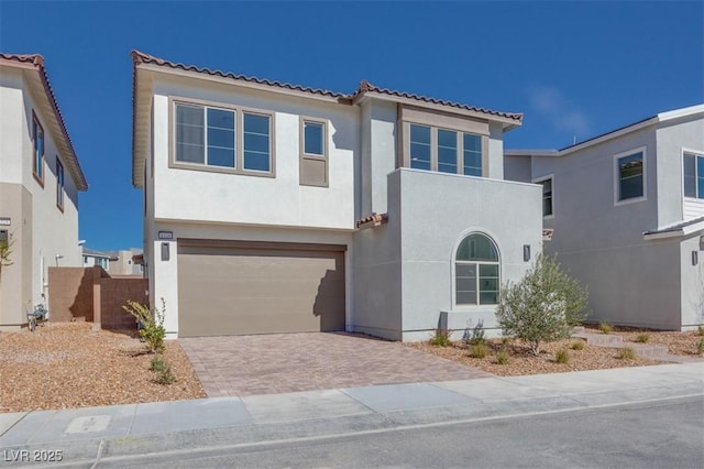 mediterranean / spanish-style house featuring an attached garage, a tiled roof, decorative driveway, and stucco siding