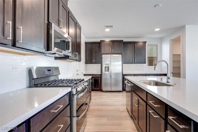 kitchen with dark brown cabinetry, light wood-style flooring, appliances with stainless steel finishes, light countertops, and a sink