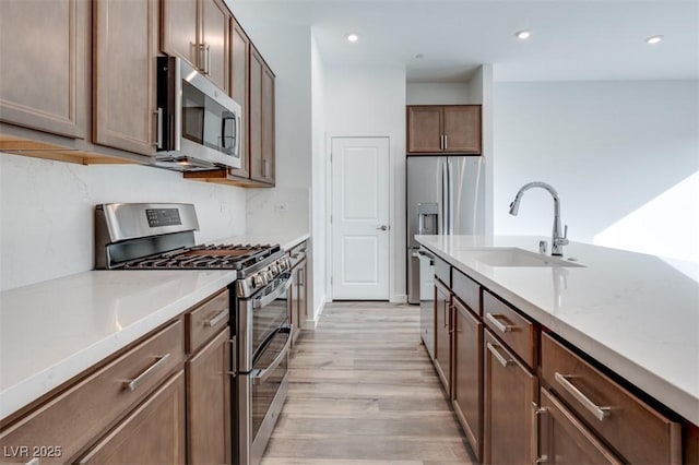 kitchen with recessed lighting, stainless steel appliances, a sink, light wood finished floors, and tasteful backsplash