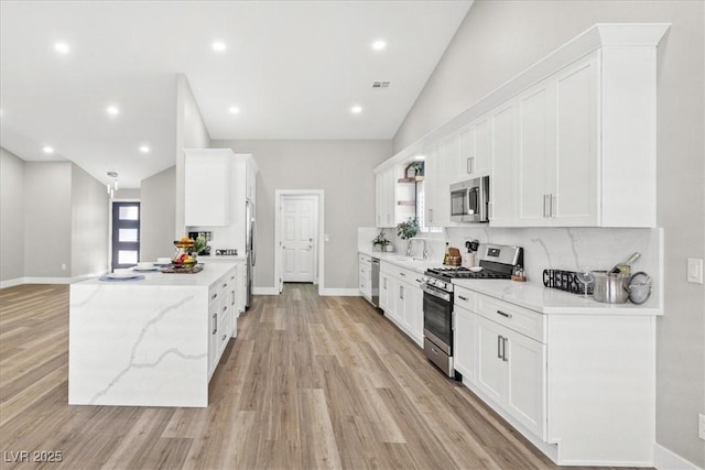 kitchen featuring stainless steel appliances, white cabinets, vaulted ceiling, decorative backsplash, and light wood finished floors