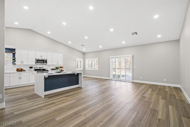 kitchen with a kitchen island with sink, white cabinetry, open floor plan, appliances with stainless steel finishes, and light wood finished floors