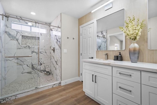 full bathroom with baseboards, vanity, a marble finish shower, and wood finished floors