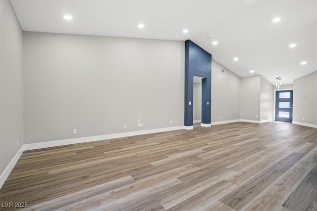 unfurnished living room featuring lofted ceiling, recessed lighting, wood finished floors, and baseboards