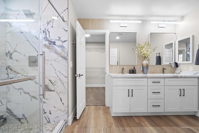 full bathroom with a sink, wood finished floors, a marble finish shower, double vanity, and a walk in closet