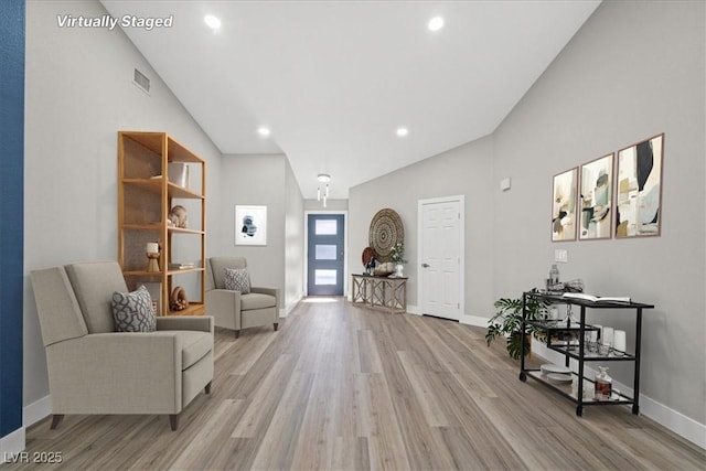 living area with high vaulted ceiling, light wood-style flooring, visible vents, and baseboards