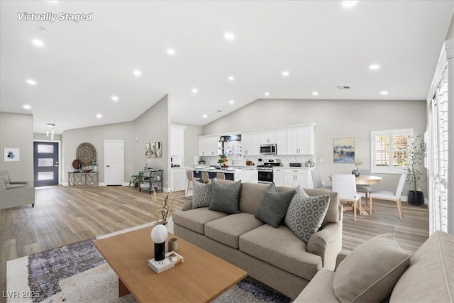 living room with light wood-style flooring, visible vents, high vaulted ceiling, and recessed lighting