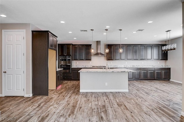 kitchen featuring visible vents, dark brown cabinetry, wall chimney range hood, and light wood finished floors