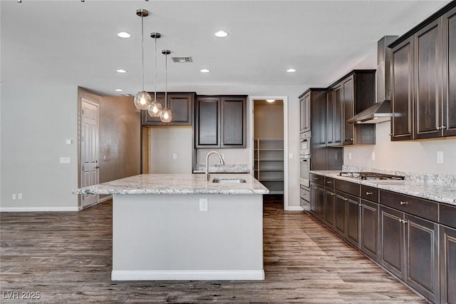 kitchen featuring wall chimney range hood, visible vents, a sink, and wood finished floors