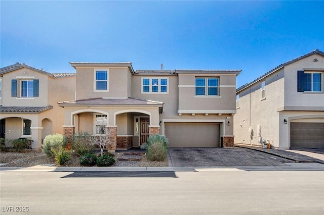 view of front facade featuring a garage, decorative driveway, stone siding, and stucco siding