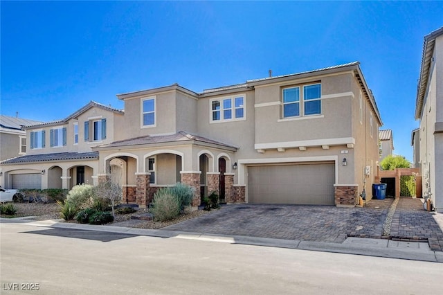 view of front of house featuring stone siding, decorative driveway, an attached garage, and stucco siding