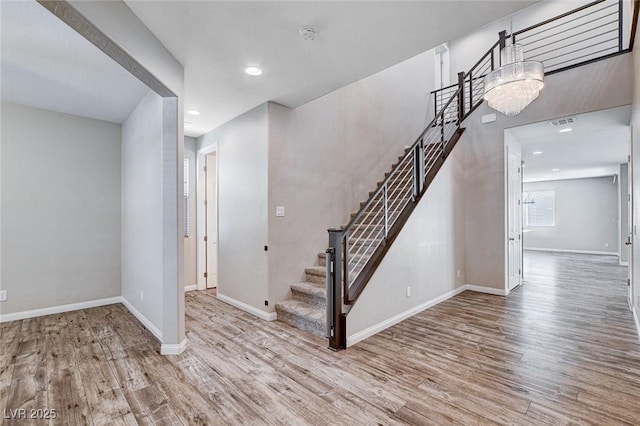 stairs with an inviting chandelier, visible vents, baseboards, and wood finished floors