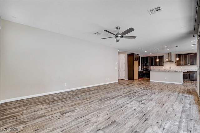 unfurnished living room featuring light wood-style floors, visible vents, a sink, and a ceiling fan