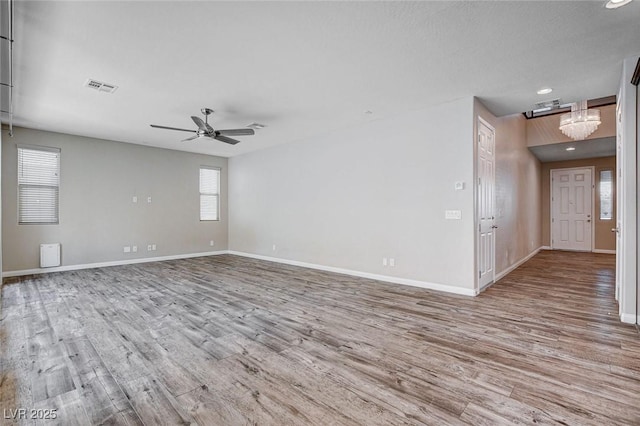 spare room featuring ceiling fan with notable chandelier, visible vents, baseboards, and wood finished floors