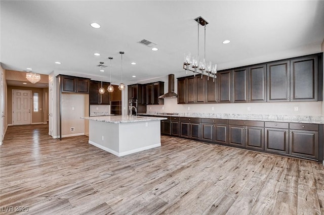 kitchen with wall chimney exhaust hood, light wood finished floors, visible vents, and dark brown cabinetry