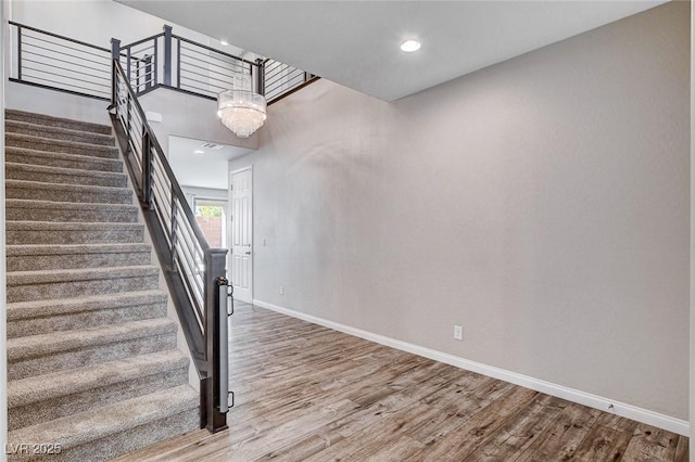 staircase featuring an inviting chandelier, baseboards, wood finished floors, and recessed lighting