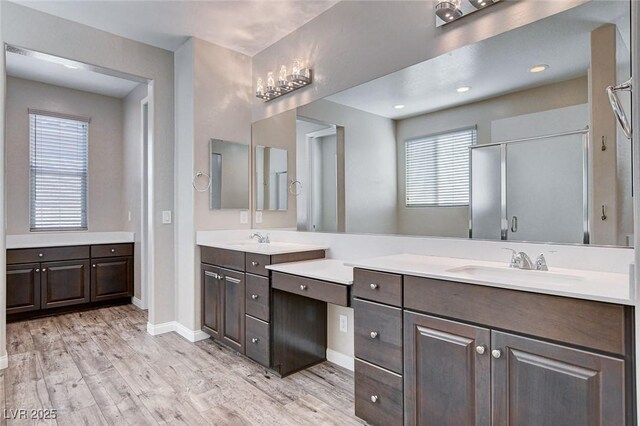 bathroom featuring two vanities, a stall shower, a sink, wood finished floors, and baseboards