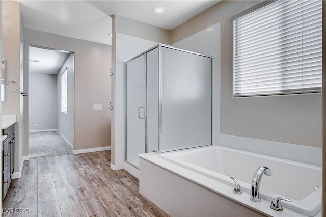 bathroom featuring a garden tub, a stall shower, vanity, wood finished floors, and baseboards