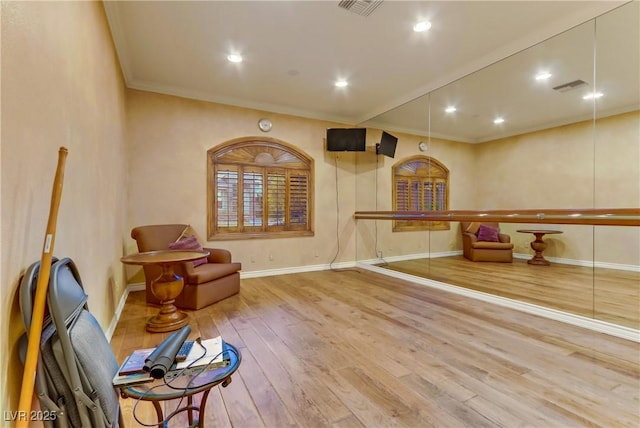 living area with wood-type flooring, visible vents, crown molding, and baseboards