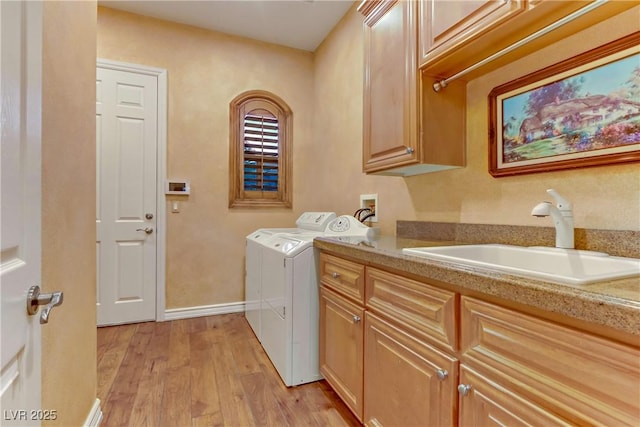 clothes washing area with washing machine and dryer, light wood-style flooring, a sink, baseboards, and cabinet space