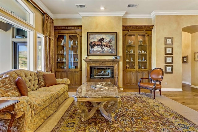 living area with arched walkways, wood finished floors, a glass covered fireplace, and visible vents