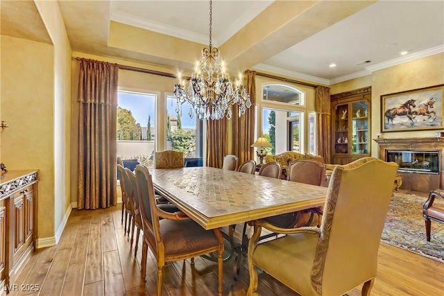 dining area featuring light wood-style flooring, baseboards, crown molding, and a glass covered fireplace