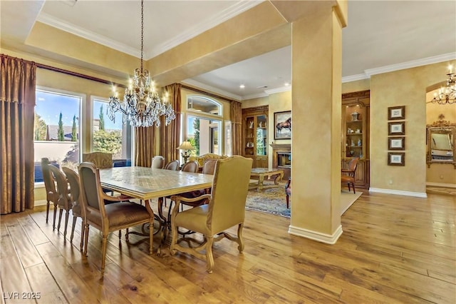 dining space featuring light wood-style flooring, crown molding, a notable chandelier, and a glass covered fireplace