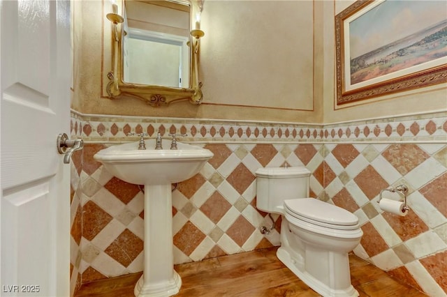 half bath featuring wainscoting, tile walls, toilet, and wood finished floors