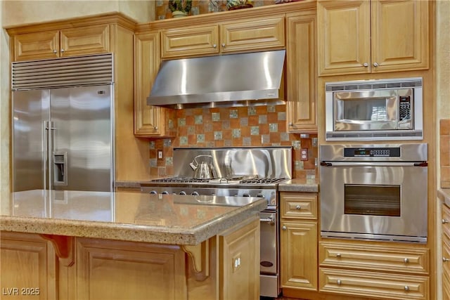 kitchen featuring light stone countertops, backsplash, under cabinet range hood, and built in appliances