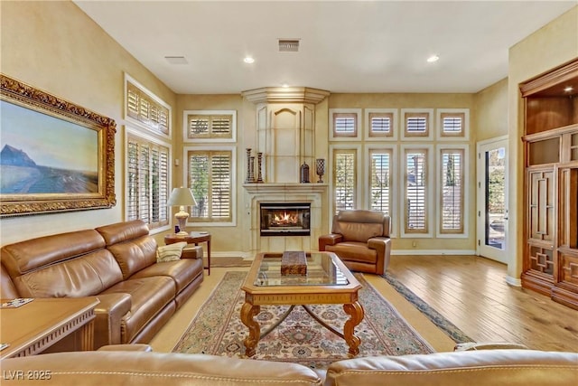 living room with a large fireplace, wood-type flooring, visible vents, and baseboards