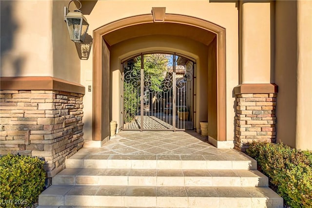 view of exterior entry with a gate and stucco siding