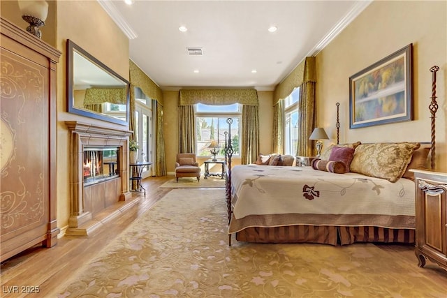 bedroom with light wood finished floors, a premium fireplace, visible vents, and crown molding