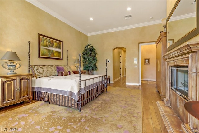 bedroom with baseboards, visible vents, arched walkways, wood finished floors, and crown molding