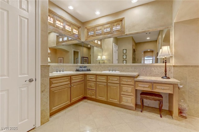 bathroom with a sink, a wainscoted wall, double vanity, and tile walls