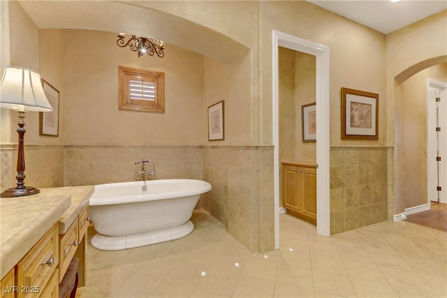 full bathroom featuring wainscoting, tile patterned floors, vanity, a freestanding tub, and tile walls