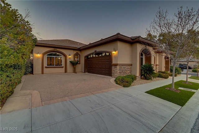 mediterranean / spanish-style house with an attached garage, driveway, stone siding, and stucco siding