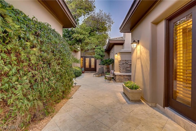 view of exterior entry featuring stone siding, a patio area, french doors, and stucco siding