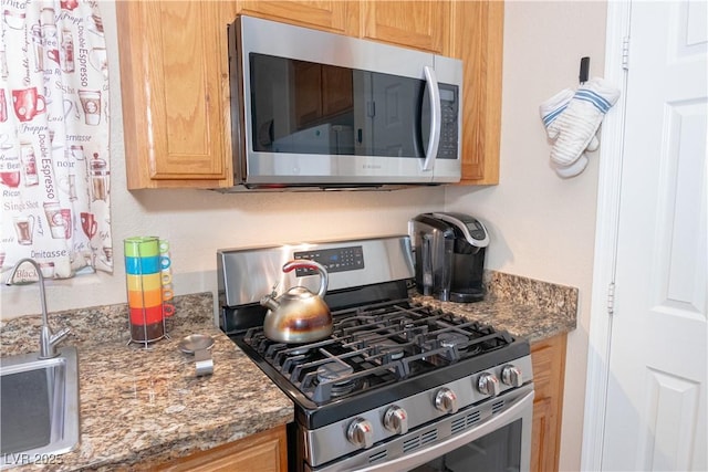 kitchen with dark stone counters, stainless steel appliances, and a sink