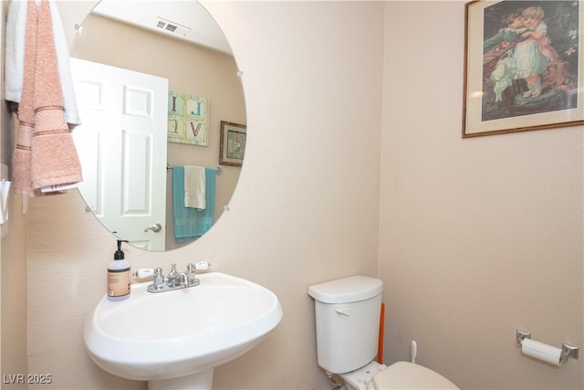 half bath featuring toilet, visible vents, and a sink