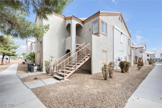 exterior space featuring stairs, central AC unit, a tile roof, and stucco siding