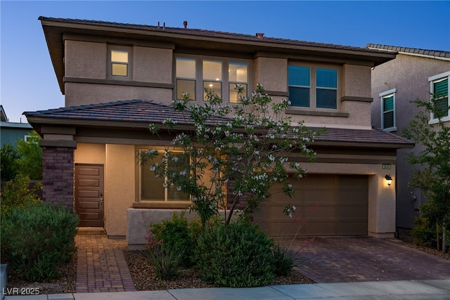 prairie-style home with a garage, decorative driveway, a tile roof, and stucco siding