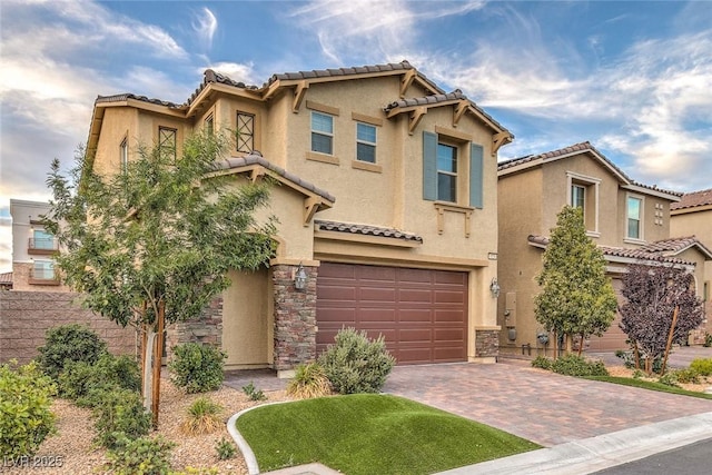 mediterranean / spanish house with a garage, stone siding, decorative driveway, and stucco siding