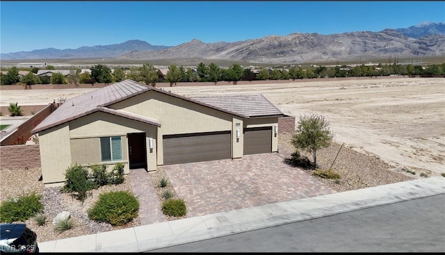 view of front of house with an attached garage, a mountain view, decorative driveway, and stucco siding