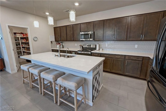 kitchen featuring light countertops, a sink, backsplash, a kitchen bar, and appliances with stainless steel finishes